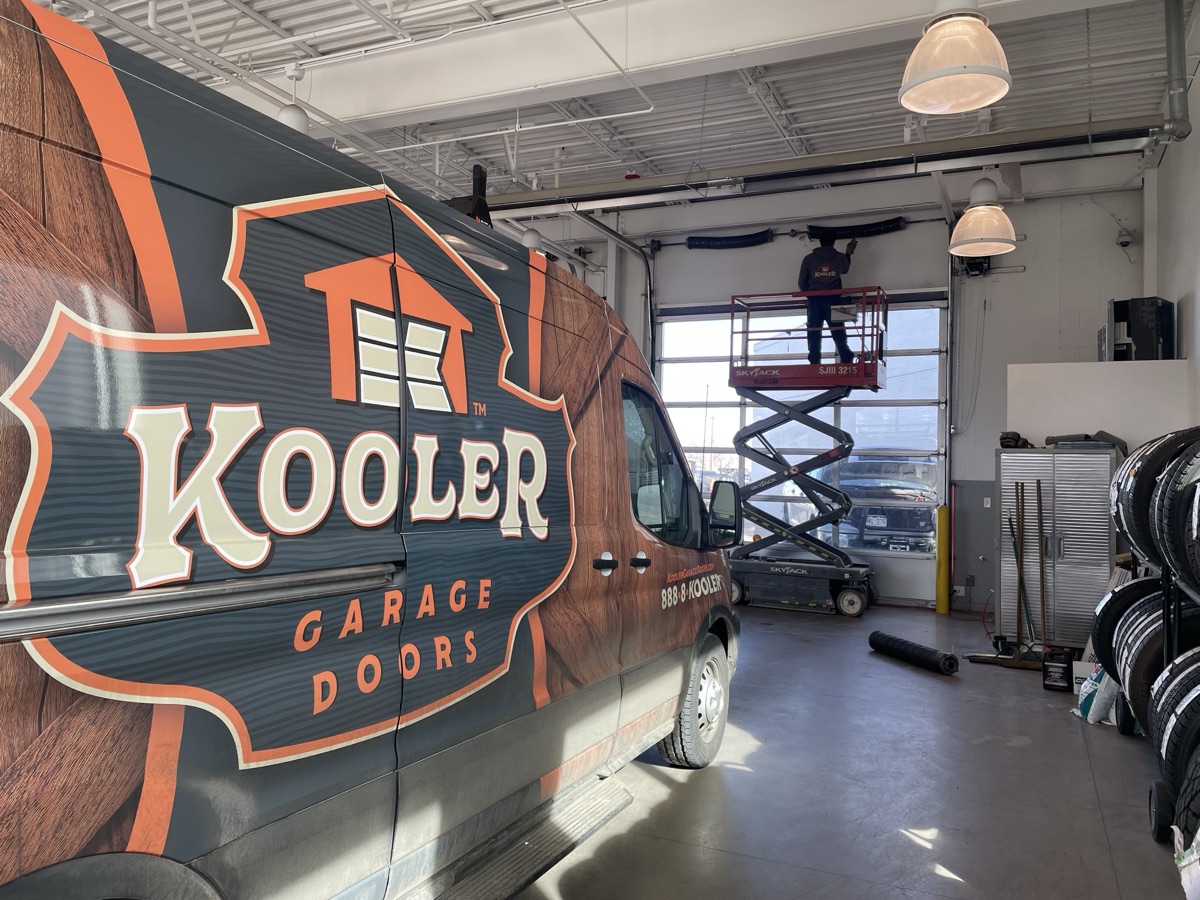 Kooler Garage Doors van inside a commercial bay with a Kraftsman on a scissor lift servicing the overhead opening