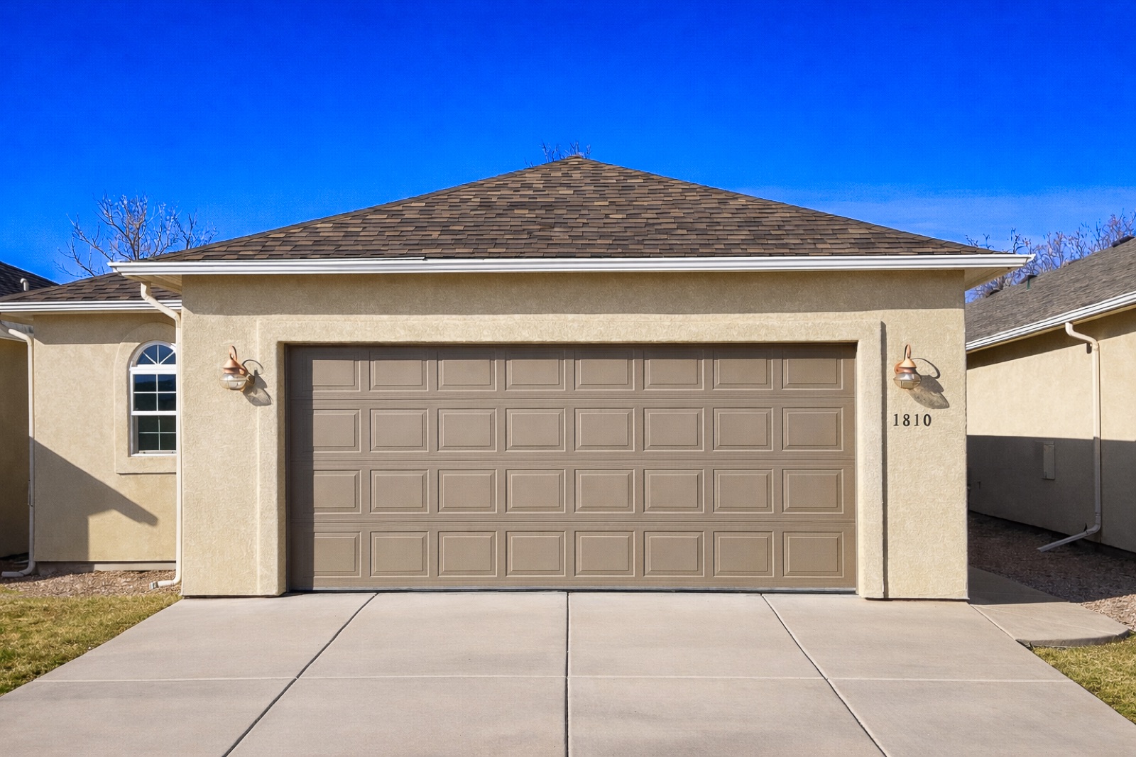 Crisp tan raised-panel double garage door on a clean stucco home