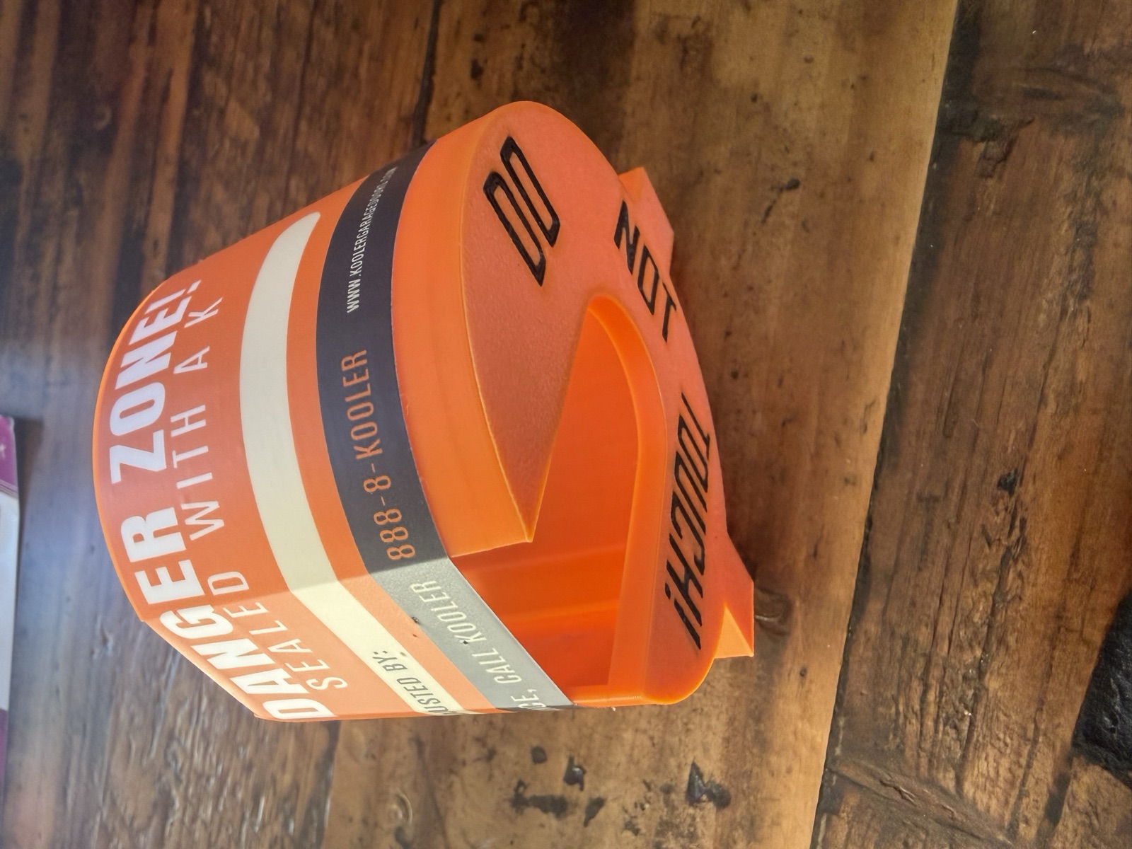 K Kap — orange plastic torsion-spring safety/warning cap with 'Danger Zone! Sealed With A K' branding and 'Do Not Touch!' warning. Currently 3D-printed in-house at Kooler.